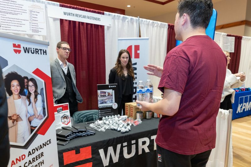 Male student in a maroon shirt talks with two employers