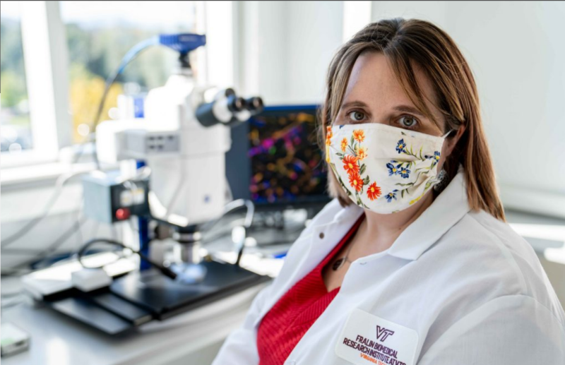 Jenny Munson wears a mask as she sits in her lab coat, in her lab