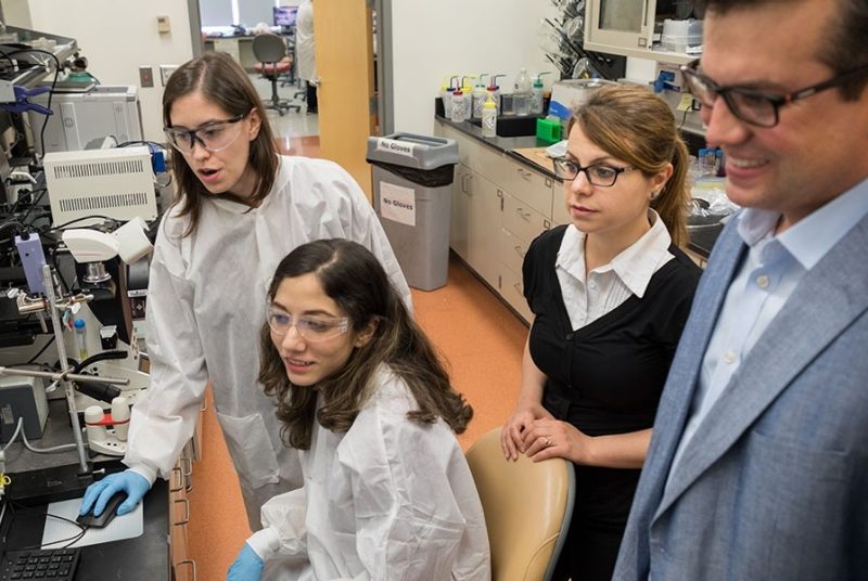 A group of BEAM grad students and faculty observe the results of an experiment in the lab