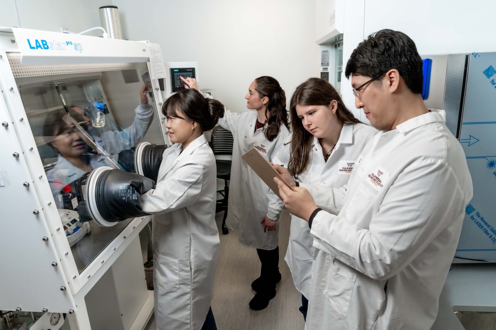 Several individuals, male and female, in lab coats, in front of a large medical machine