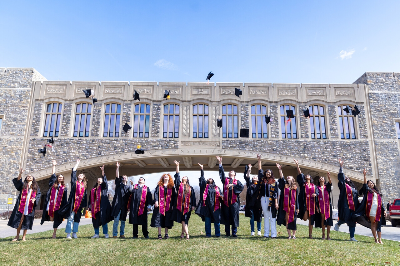 Graduates in caps and gowns tossing caps into the air in front of Torgesen bridge