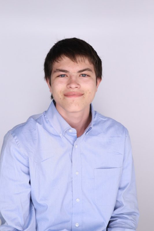 Young man with short, dark hair, wearing a light blue button down dress shirt.