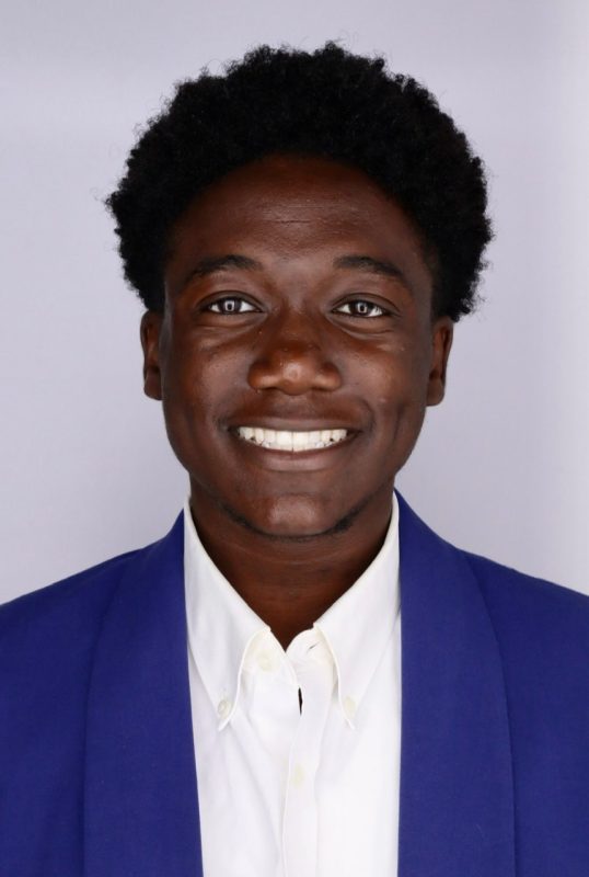 Young black man, with short hair, dark blue jacket and a white collared shirt.