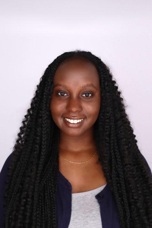 Young black woman with long, dark, curly hair, wearing a dark cardigan with a gray shirt.