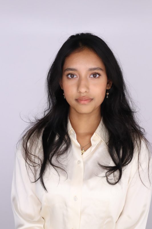 Young woman with long, dark hair, wearing a cream collared shirt.