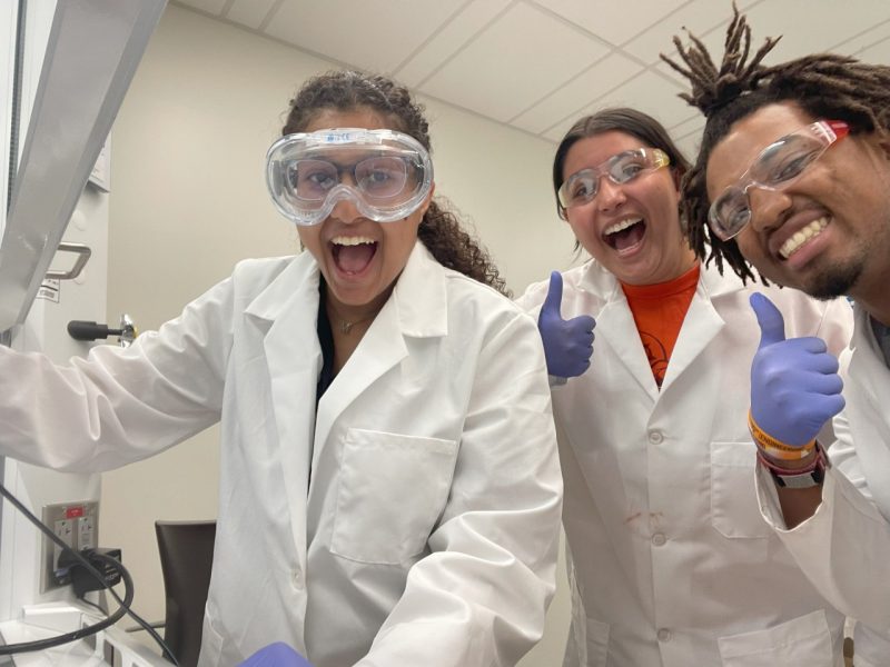 Group of students wearing lab coats and goggles, laughing.