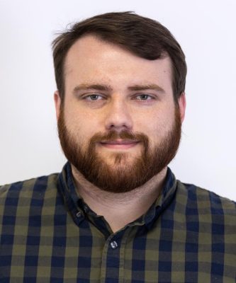 Headshot of Joshua Howard, man with dark hair and beard wearing a dark checked shirt