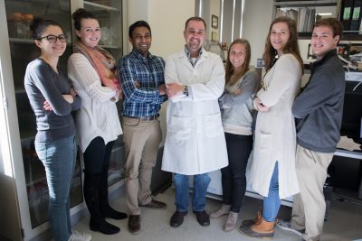 Dr Verbridge stands in the middle of a group -- his students -- in his biomedical engineering lab