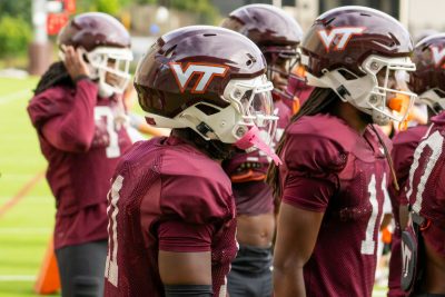 Image of multiple Virginia Tech football players wearing maroon and white uniforms, helmets with VT on them in white.